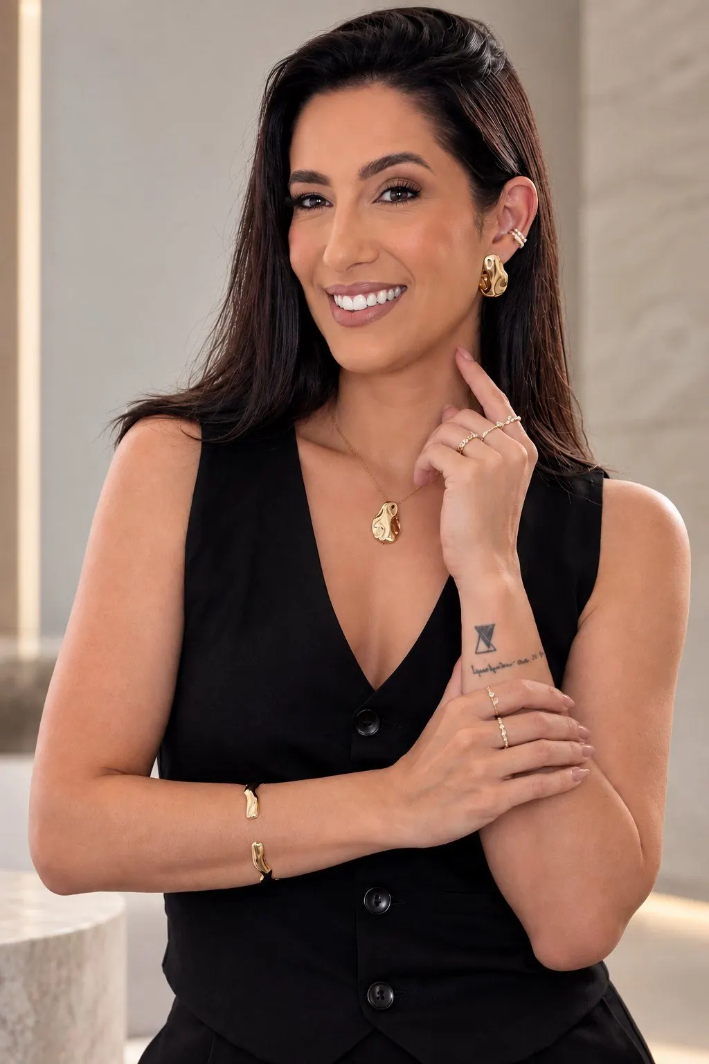 Ju Manzalli sorrindo, usando brinco, colar, pulseira e anéis dourados da Manzalli